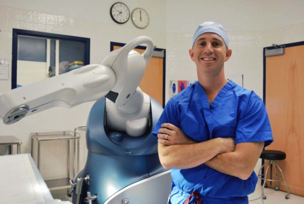 Dr. Scott Goldsmith posing in front of the robot used to assist in joint replacement procedures